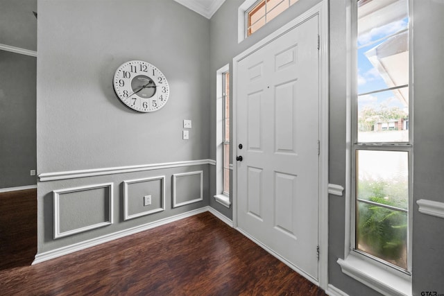 foyer entrance with dark wood-type flooring, a decorative wall, crown molding, and wainscoting