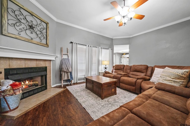 living area featuring a tiled fireplace, wood finished floors, crown molding, baseboards, and ceiling fan