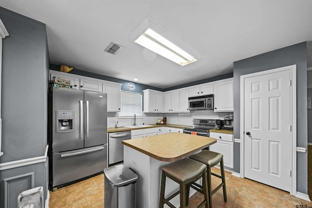 kitchen featuring visible vents, a breakfast bar, a sink, white cabinetry, and stainless steel appliances