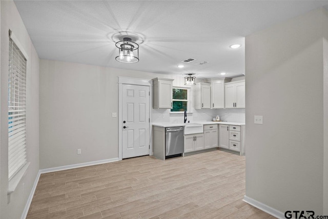 kitchen with a notable chandelier, sink, stainless steel dishwasher, white cabinetry, and light hardwood / wood-style flooring