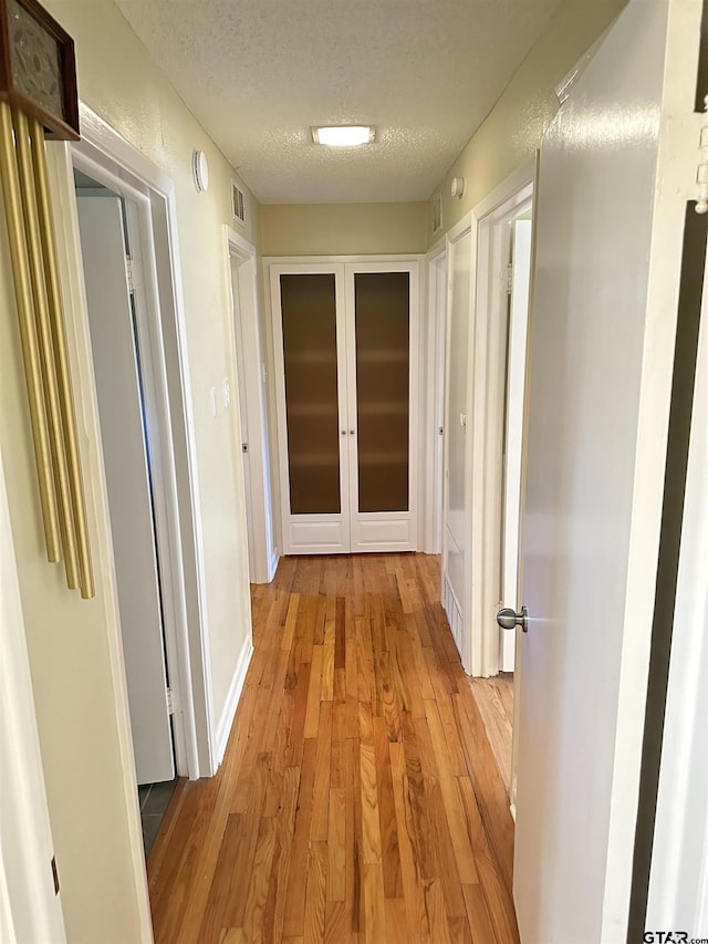 hall with light hardwood / wood-style floors, a textured ceiling, and french doors