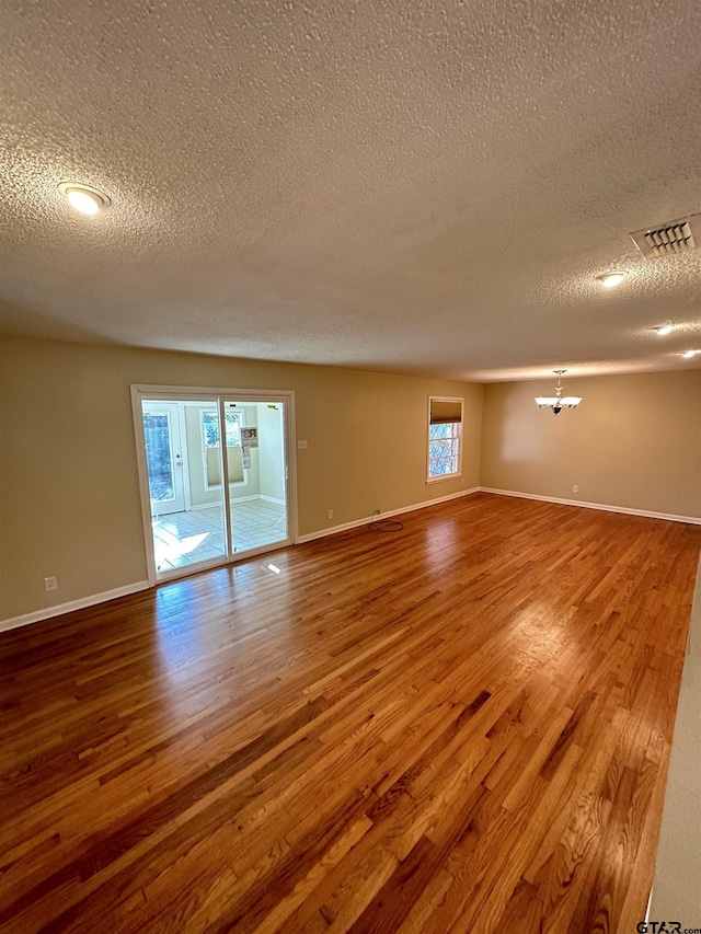 empty room with hardwood / wood-style floors, a chandelier, and a textured ceiling