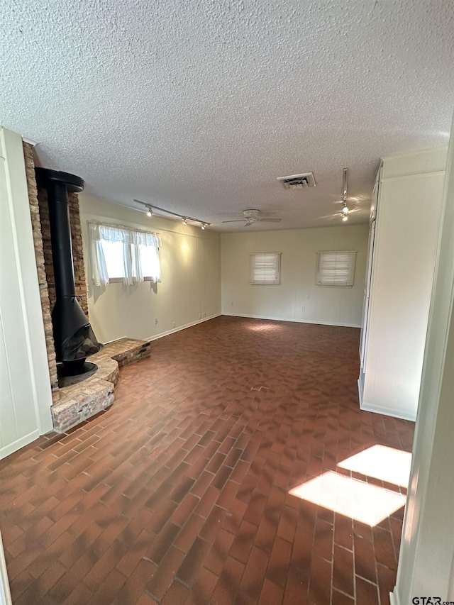 unfurnished living room featuring a wood stove, ceiling fan, and a textured ceiling