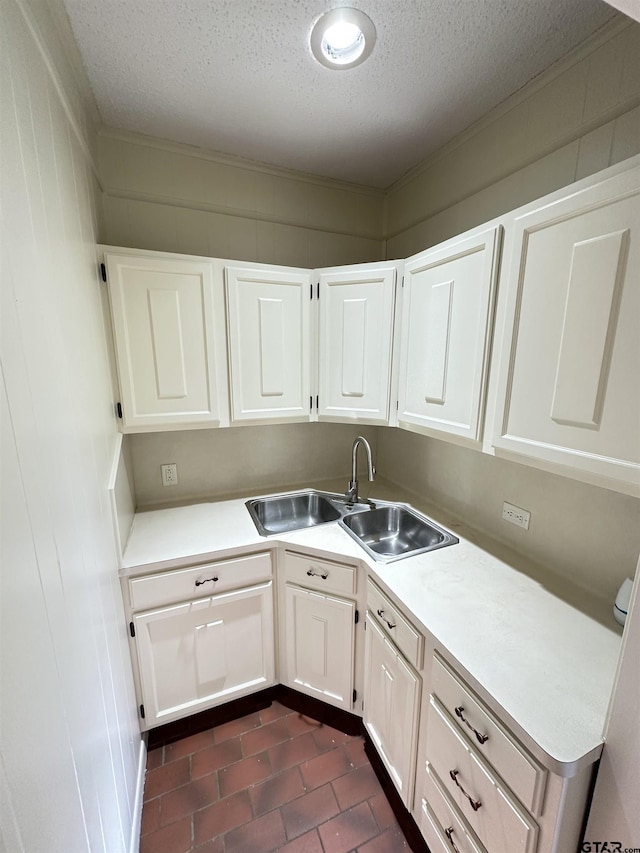 kitchen featuring sink, a textured ceiling, white cabinets, and crown molding