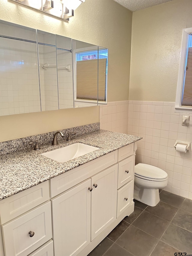 bathroom featuring tile patterned floors, tile walls, a textured ceiling, toilet, and vanity