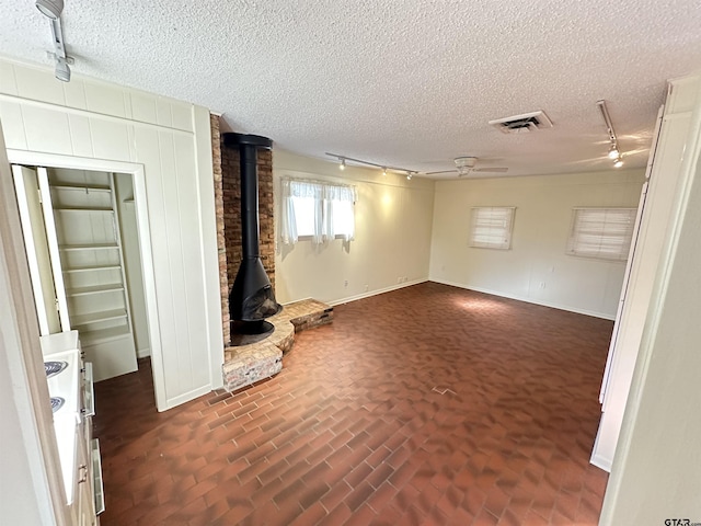 unfurnished living room with a wood stove, a textured ceiling, and track lighting