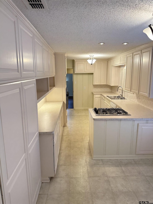 kitchen with sink, a textured ceiling, kitchen peninsula, and stainless steel gas cooktop