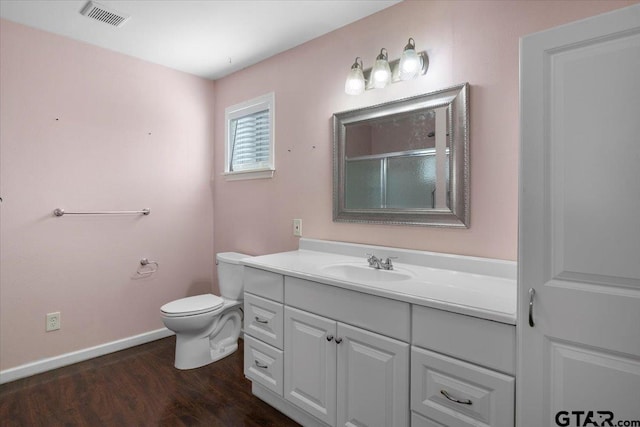 bathroom featuring wood-type flooring, a shower with door, toilet, and vanity