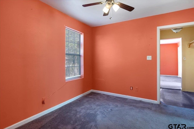 empty room featuring ceiling fan, dark carpet, and a healthy amount of sunlight