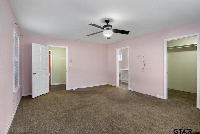 unfurnished bedroom with a walk in closet, ensuite bath, dark colored carpet, a closet, and ceiling fan