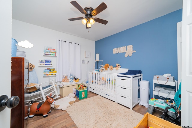 bedroom with a nursery area, wood finished floors, and a ceiling fan