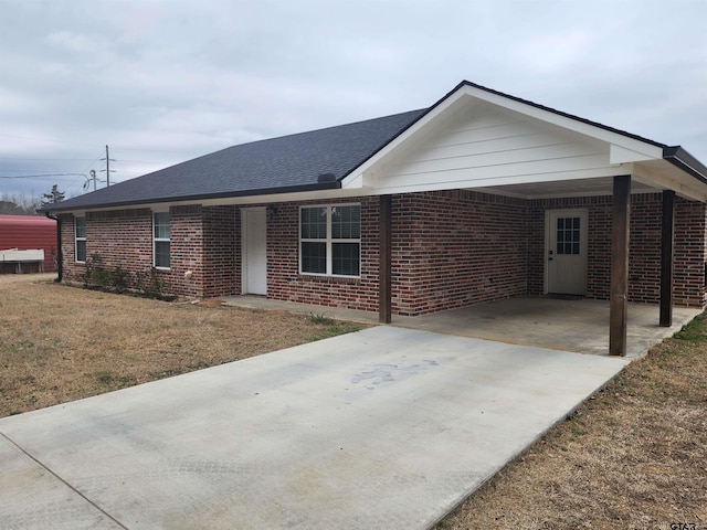 ranch-style home featuring concrete driveway, brick siding, roof with shingles, and an attached carport