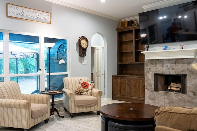 living room featuring a tile fireplace, baseboards, crown molding, arched walkways, and light wood finished floors