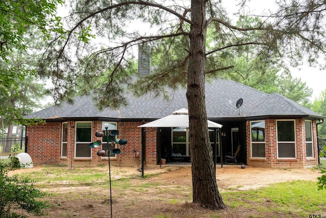 rear view of property featuring a gazebo, brick siding, fence, and a shingled roof