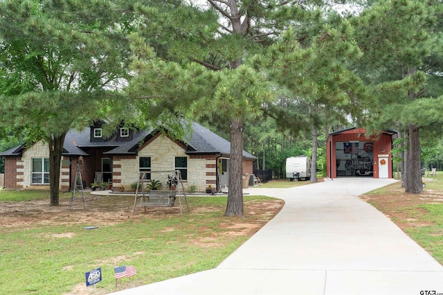 view of front facade with an outbuilding, a front yard, stone siding, a shingled roof, and concrete driveway