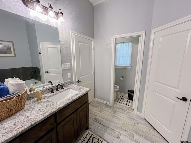 full bathroom featuring vanity, toilet, wood finished floors, a textured wall, and baseboards