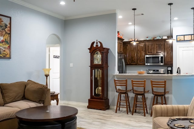 living room with baseboards, crown molding, light wood-style floors, visible vents, and arched walkways
