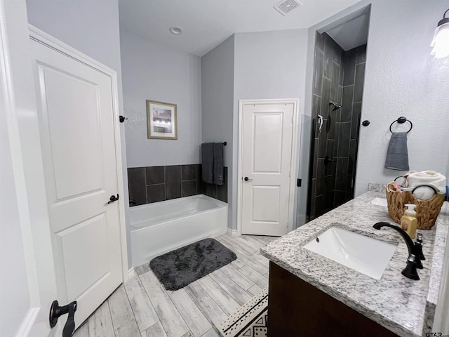 full bath with visible vents, a sink, double vanity, wood finished floors, and a garden tub