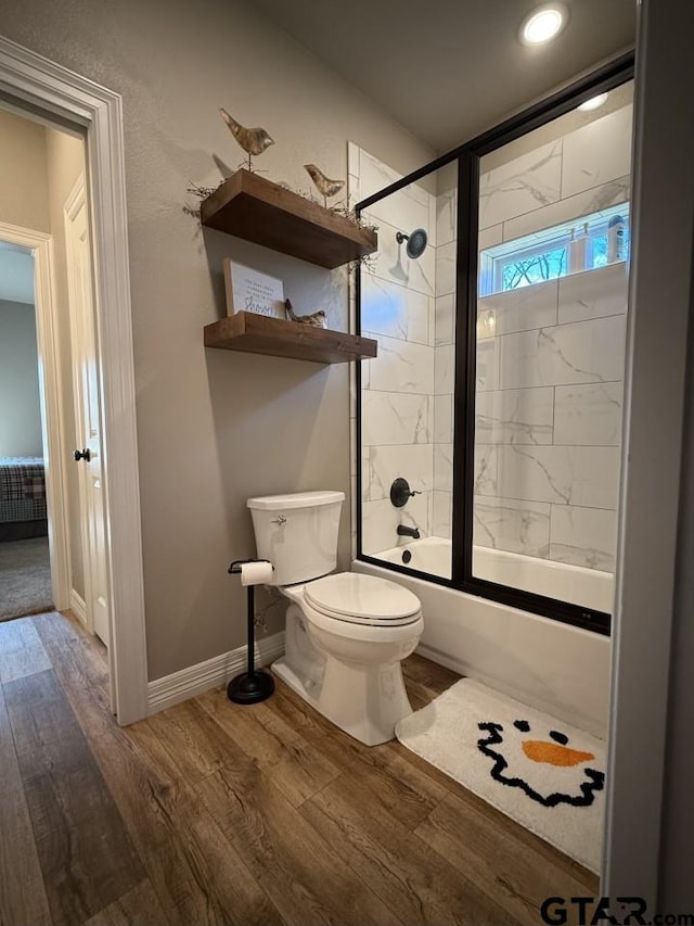 bathroom with hardwood / wood-style flooring, toilet, and shower / bath combination with glass door