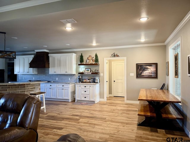 kitchen with light wood-type flooring, premium range hood, tasteful backsplash, crown molding, and white cabinetry