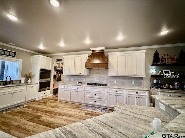 kitchen with premium range hood, light stone counters, ornamental molding, sink, and white cabinets