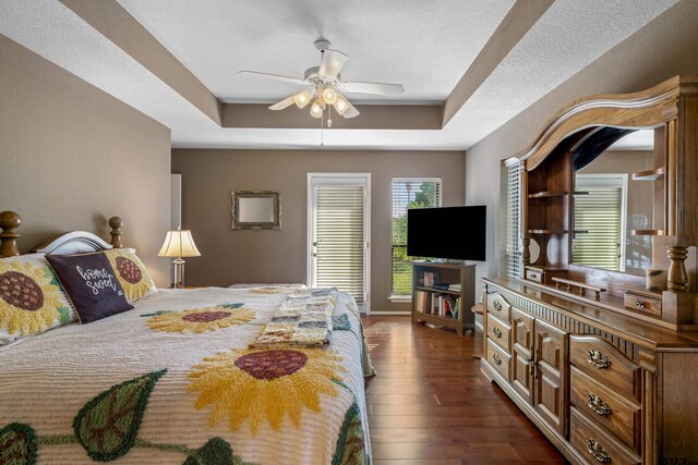 bedroom featuring a textured ceiling, ceiling fan, a raised ceiling, and dark wood-type flooring