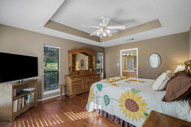 bedroom featuring ceiling fan, dark hardwood / wood-style floors, a raised ceiling, and connected bathroom