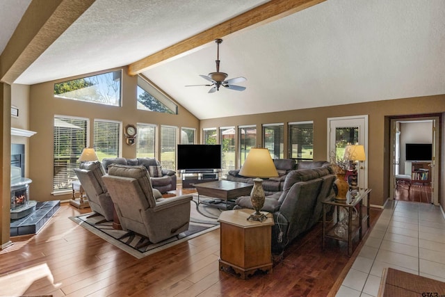 living room with a wood stove, ceiling fan, a textured ceiling, beamed ceiling, and light hardwood / wood-style floors