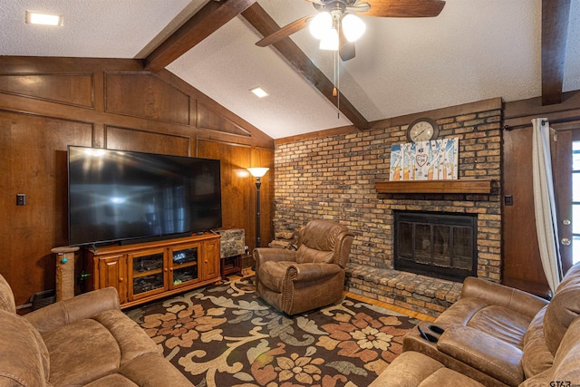 living room with ceiling fan, vaulted ceiling with beams, wooden walls, a textured ceiling, and a brick fireplace