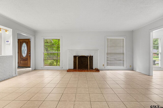 708 E Loftin St, Tyler, TX 75701 - unfurnished living room featuring a textured ceiling, a brick fireplace, light tile patterned floors, and crown molding