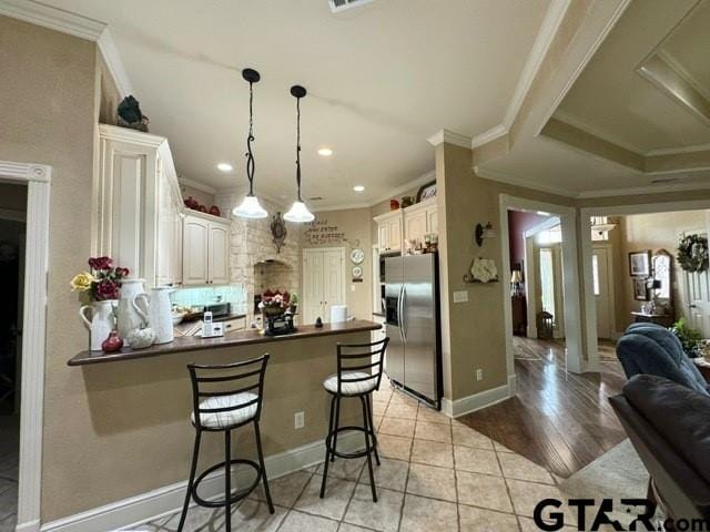kitchen featuring dark countertops, a peninsula, ornamental molding, and stainless steel fridge