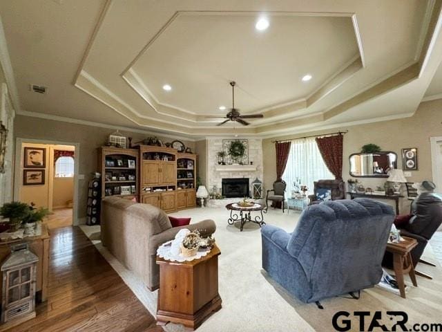 living room with a ceiling fan, crown molding, a fireplace with raised hearth, a raised ceiling, and visible vents