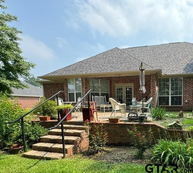back of property featuring brick siding, a patio area, french doors, and roof with shingles