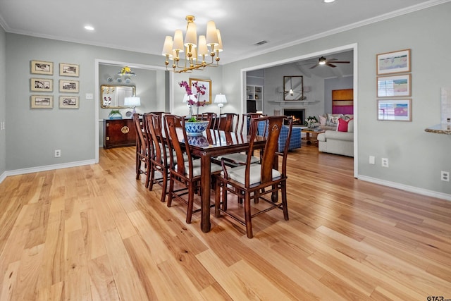 dining room with light wood-style flooring, ornamental molding, a lit fireplace, baseboards, and ceiling fan with notable chandelier