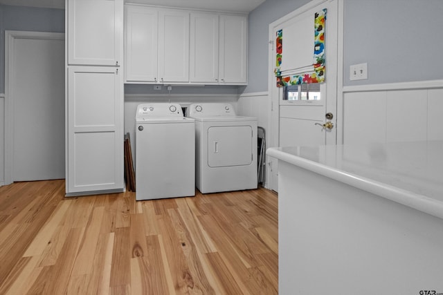 laundry area with light wood-type flooring, a wainscoted wall, cabinet space, and washer and clothes dryer