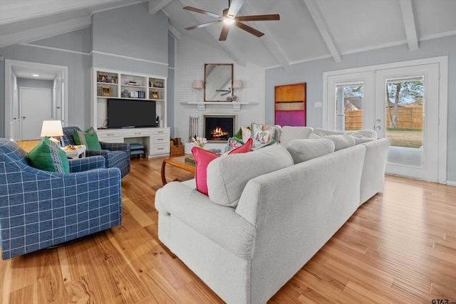 living room featuring vaulted ceiling with beams, ceiling fan, french doors, a brick fireplace, and light wood finished floors