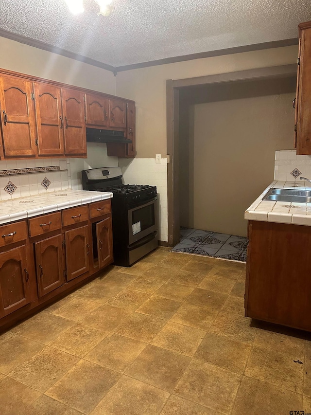 kitchen with a textured ceiling, black range with gas cooktop, decorative backsplash, sink, and tile countertops