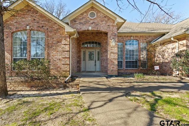 doorway to property with brick siding and roof with shingles