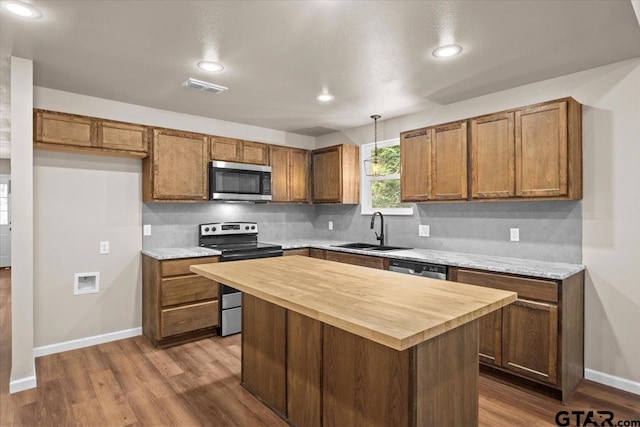 kitchen featuring hardwood / wood-style floors, hanging light fixtures, sink, a kitchen island, and appliances with stainless steel finishes