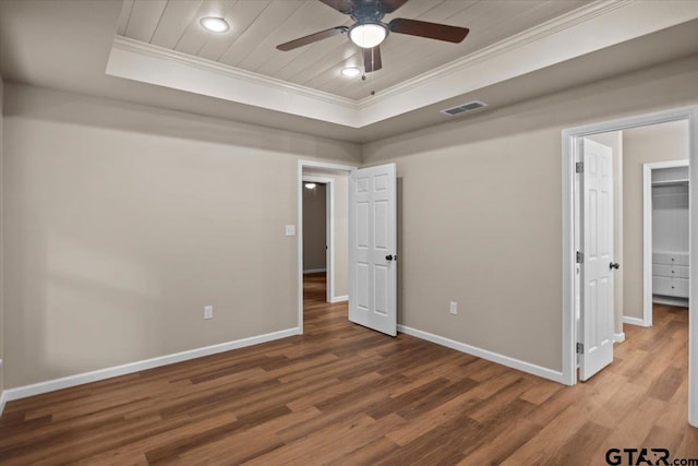 unfurnished bedroom featuring a spacious closet, crown molding, a raised ceiling, hardwood / wood-style floors, and ceiling fan