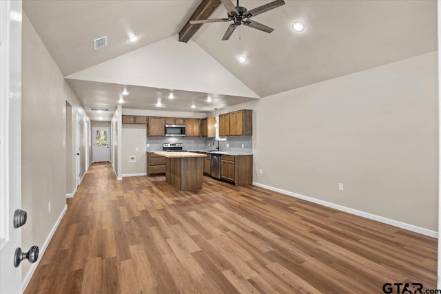 kitchen featuring vaulted ceiling with beams, stainless steel appliances, a kitchen island, sink, and hardwood / wood-style floors