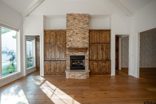 21585 Syrah Ln, Tyler, TX 75703 - unfurnished living room with beam ceiling, light wood-style flooring, a stone fireplace, high vaulted ceiling, and baseboards