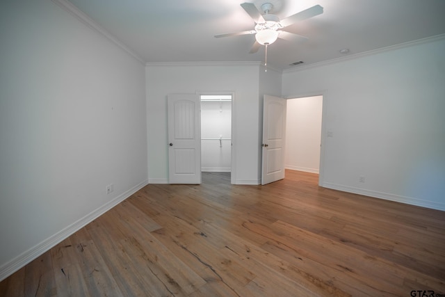 unfurnished bedroom featuring ceiling fan, crown molding, light wood-type flooring, and a spacious closet