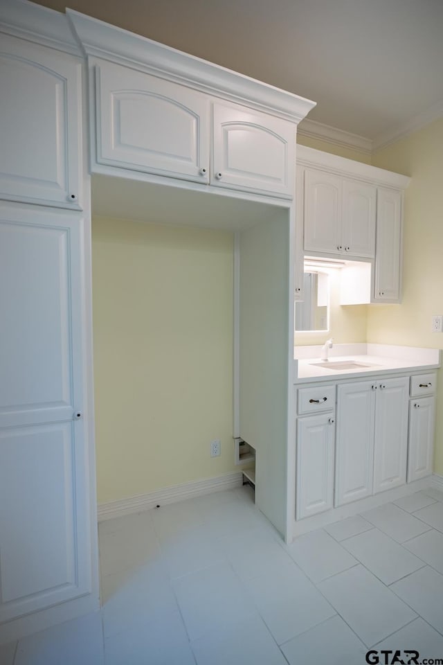 kitchen featuring white cabinets, ornamental molding, sink, and light tile patterned flooring