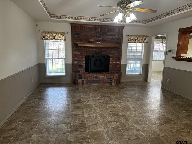 unfurnished living room with ceiling fan, crown molding, a fireplace, and a tray ceiling