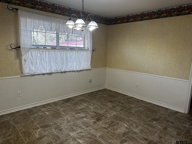 unfurnished room featuring an inviting chandelier, wainscoting, and wallpapered walls