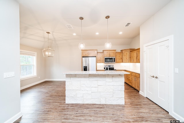 kitchen with appliances with stainless steel finishes, light wood-type flooring, a kitchen island, and pendant lighting