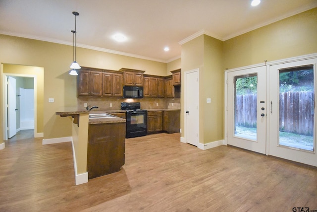 kitchen featuring black appliances, kitchen peninsula, a breakfast bar area, decorative light fixtures, and light wood-type flooring