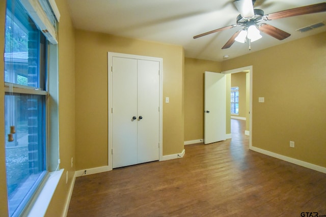 unfurnished bedroom with wood-type flooring, multiple windows, ceiling fan, and a closet