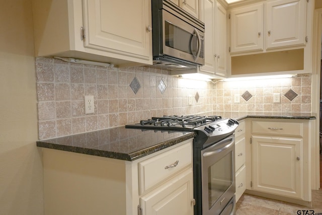 kitchen featuring appliances with stainless steel finishes, dark stone countertops, backsplash, and light tile patterned floors